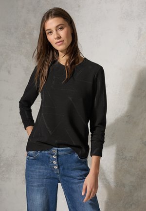 Sweatshirt noir avec un motif géométrique texturé, col rond, et manches longues, associé à un jean taille haute bleu clair avec fermeture à boutons.
