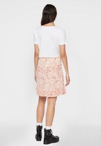 Witte T-shirt met korte mouwen, gecombineerd met een lichtroze bloemenrok met een rucheszoom, gedragen met zwarte stevige laarzen en witte sokken.