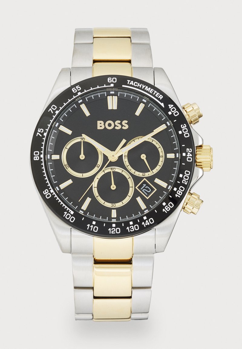Black dial watch with gold accents, stainless steel and gold-toned band, tachymeter scale, chronograph functions, and date display.