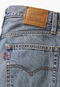Poche arrière d'un jean Levi's bleu avec un patch en cuir de la marque et une étiquette rouge Levi's sur la couture latérale.