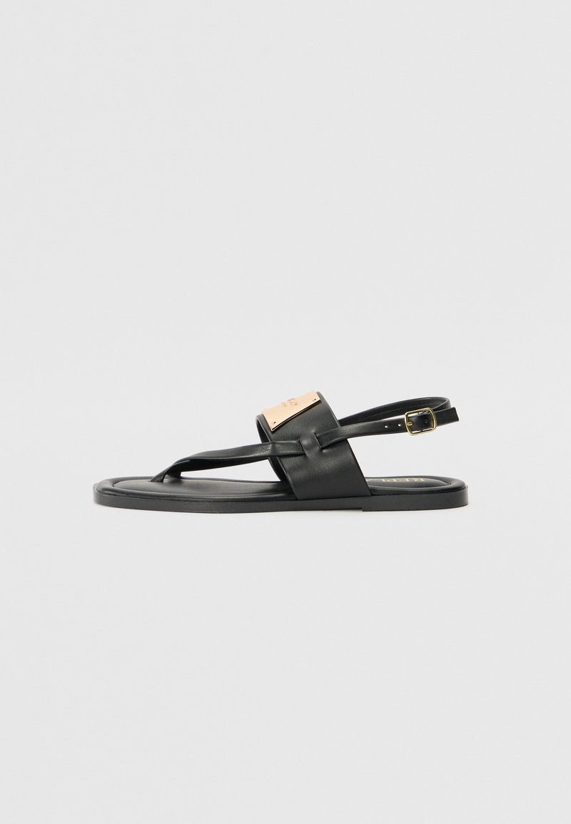 Sandale negre din piele cu talpă plată, având un design cu baretă frontală, curea la gleznă ajustabilă și un accent din metal auriu mat.