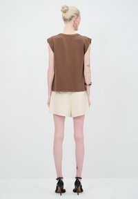 Top sin mangas marrón con hombros estructurados; combinado con pantalones cortos crema; usado con sandalias de tacón negras; diseño minimalista.