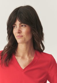 Rød v-hals t-shirt lavet af blødt stof, med korte ærmer og en afslappet pasform. Enkel design uden synlige mønstre eller dekorationer.