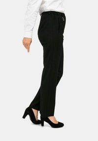 Zwarte broek met een ontspannen pasvorm en elastische tailleband, voorzien van zijzakken en een gladde textuur, gecombineerd met zwarte suède hakken.