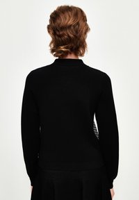 Der schwarze Strickpullover hat einen eleganten Kragen, lange Ärmel und eine strukturierte Rückseite mit einem kontrastierenden weißen Muster. Insgesamt glatte Finish.