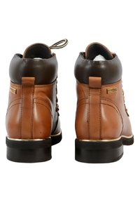 Stivali ankle in pelle marrone con colletto in pelle marrone scuro, dettagli con occhielli e suola in gomma nera. Presentano un linguetta posteriore e un logo dorato.