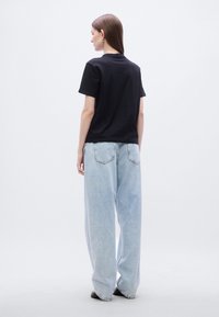 Μαύρο βαμβακερό t-shirt συνδυασμένο με ανοιχτό μπλε, χαλαρής εφαρμογής τζιν παντελόνι. Τα κάτω άκρα είναι ελαφρώς ξεφτισμένα. Μινιμαλιστικός σχεδιασμός χωρίς εμφανή γραφικά.