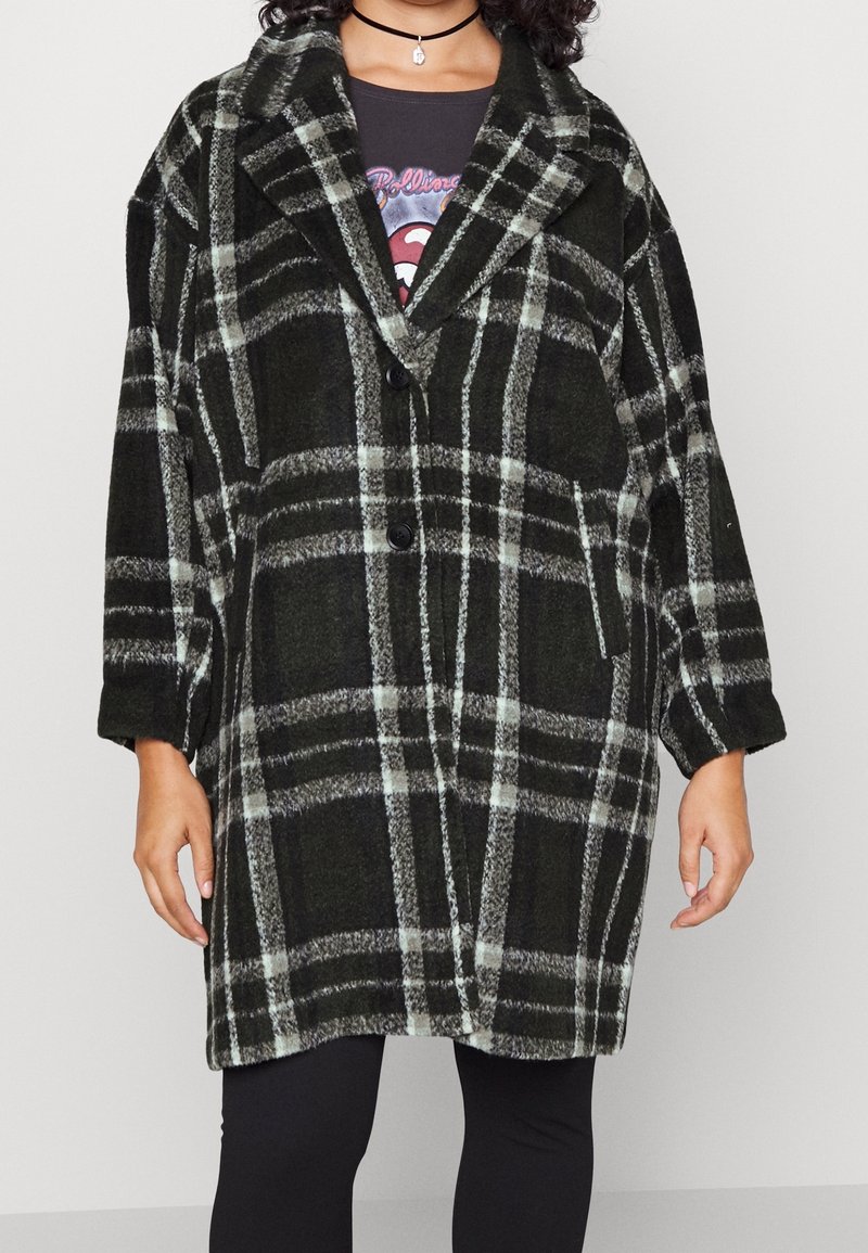 Zwart en groene geruite oversized jas met een geknipte kraag, twee voorzakken en knoopsluiting. Stof lijkt zacht en heeft een gestructureerde uitstraling.