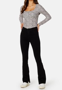 Långärmad, åtsittande bodysuit i vitt med svarta blommönster, i kombination med högmidjade svarta utsvängda jeans och vita sneakers.