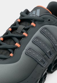 Hall hall spordijalats tekstureeritud materjaliga, kolm kummist triipu, must võrkmaterjalist ülaltosa, oranžid paelad ja nähtav polsterdatud tald.