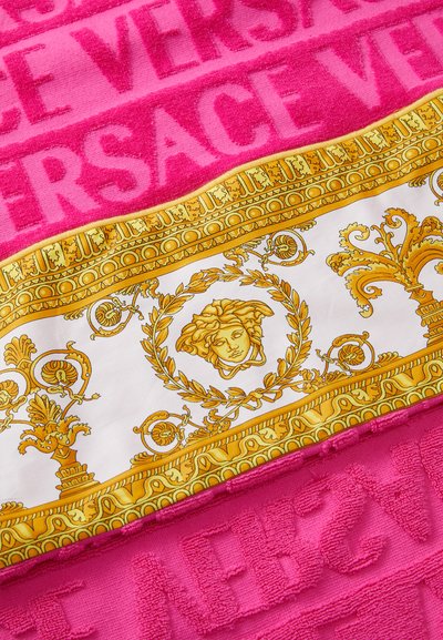 Serviette de plage en terrycloth rose avec le texte "VERSACE" en relief, surmontée d'un design baroque en or et blanc avec un médaillon au centre.