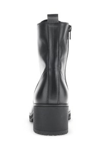 Bottine en cuir noir avec un bout arrondi, une fermeture éclair à l'arrière, un talon empilé et une texture lisse, ornée d'accents de couture verticale.