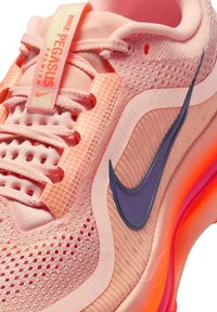 Zapatilla de running Nike Pegasus rosa con parte superior de malla, cordones rosas y logo de Nike morado, que cuenta con una suela acolchada naranja.