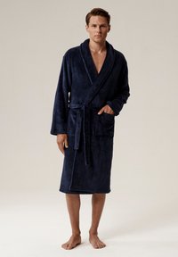 Granatowy szlafrok wykonany z miękkiego, teksturowanego materiału; posiada kołnierz szala, boczne kieszenie i pasujący pasek. Kończy się tuż nad kostką.