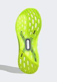 Suela de zapato de un amarillo-verde brillante con un patrón de agarre texturizado, con una amortiguación blanca visible a través de un corte ovalado etiquetado como "SISTEMA DE TORSIÓN".