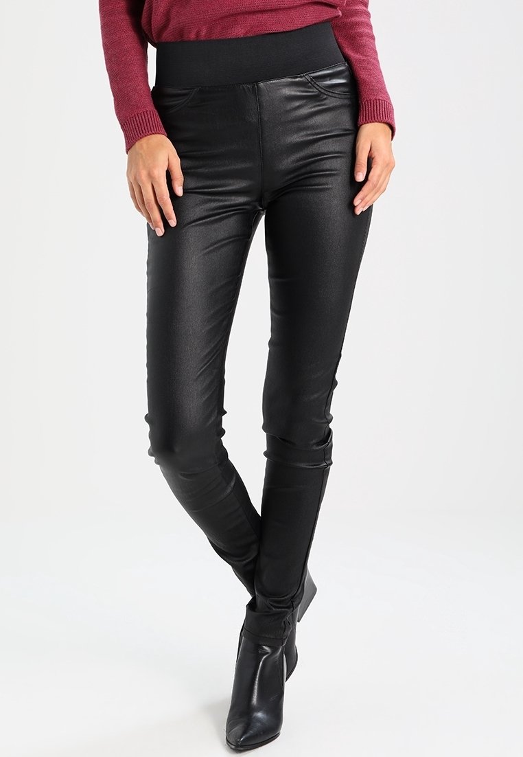 Femme portant des leggings en simili cuir noir avec une taille haute élastique et des bottines noires, assortis à un haut rouge à manches longues.