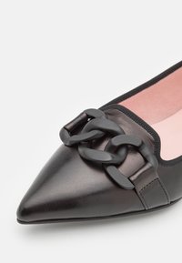Ballerines noires en cuir pointu avec un intérieur rose, présentant un accent de chaîne noire épaisse sur le dessus. Texture lisse, design élégant.