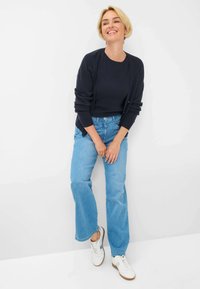 Marineblauw geribd sweater, lichtblauwe wijde jeans en witte sneakers. De outfit heeft een ontspannen pasvorm met een casual, comfortabele uitstraling.