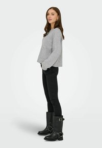 Lysegrå strikket sweater med rund halsudskæring og frontlomme, parret med sorte tætsiddende jeans og knæhøje sorte støvler med dekorativt hardware.