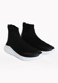 Czarne dzianinowe buty wsuwane z wysoką cholewką, z białą amortyzującą podeszwą i czerwonymi akcentami na pięcie oraz logo.