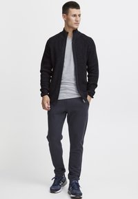 Mörk stickad zip-up tröja, grå t-shirt och mörka sweatpants. Robust textur, tajt design och matchande sneakers för en enhetlig look.