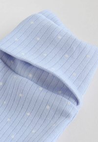 Chaussette bleu clair côtelée avec de petits pois blancs, repliée au niveau du bord sur un fond uni clair.