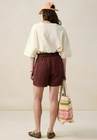 T-shirt oversize beige, shorts bordeaux avec taille élastique, ballerines imprimé léopard et sac fourre-tout rayé avec accents multicolores.