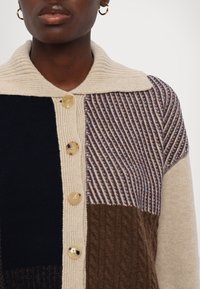 Knopencardigan met beige, marineblauwe, bruine en paarse gebreide secties, geribbelde textuur en ronde kraag met vijf ronde knopen.