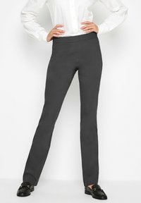Pantalones ajustados gris oscuro con una tela suave y elástica y una cinturilla ancha; combinados con mocasines negros y una camisa blanca de botones.
