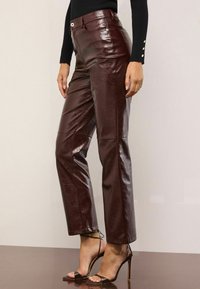 Burgundijas augsto jostasvietu ādas bikses ar gludu apdari un smalkiem dūrieniem, apvienotas ar siksniņu augstpapēžu sandālēm.