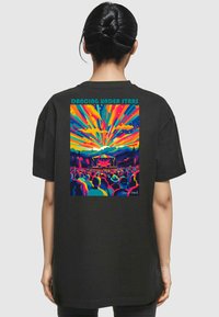 Black cotton t-shirt featuring a vibrant graphic of abstract concert scene with colorful rays and figures. Text reads "Dancing Under Stars."