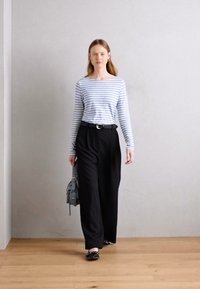 Prugasta majica dugih rukava u svijetloplavoj i bijeloj boji, crne krojene široke hlače, crne balerinke, siva torba preko ramena, minimalistički dizajn, elegantan izgled.
