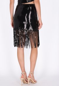 Fekete flitteres szoknya rojtos részletekkel, testhezálló sziluettel és sima textúrával. Magas hasítékkal és bokapántos magassarkúval kiemelve.