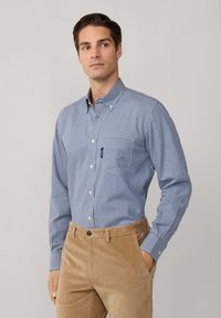 Camisa de cuadros azul y blanca con cuello y bolsillo en el pecho, combinada con pantalones de pana en color beige con una textura acanalada.