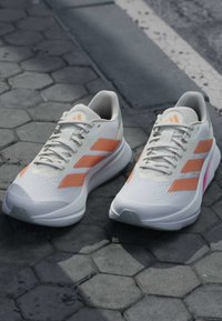 Chaussures de course blanches et orange clair avec des lacets sur un trottoir pavé en pierre près d'un bord de trottoir et du bord de la route.