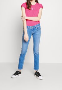 Pink fitted T-shirt with logo, light blue slim jeans, and black low-top sneakers. Simple design, smooth texture, casual style.