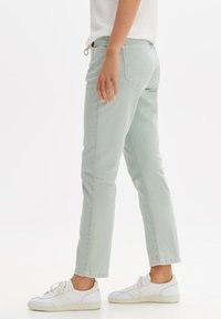 Jeans verde chiaro a gamba dritta con vita media, tasche posteriori e una texture morbida, abbinati a sneaker sportive bianche.