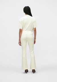 Εκρού, εφαρμοστό σύνολο με κοντά μανίκια και καμπάνα παντελόνι. Ομαλή υφή, μίνιμαλ σχεδιασμός, με πίσω τσέπη. Παπούτσια με τακούνι.