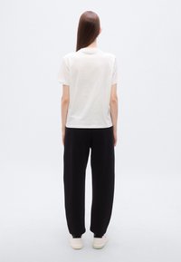 Λευκό βαμβακερό μπλουζάκι με άνετη εφαρμογή, ολόλευκη πλάτη, συνδυασμένο με μαύρη φαρδιά φόρμα και λευκά αθλητικά παπούτσια, μίνιμαλ σχεδιασμός, χωρίς ορατά σχέδια.