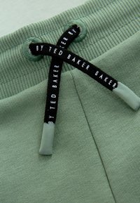 Zelené bavlnené šortky s rebrovaným pásom a čiernou šnúrkou na sťahovanie. Na šnúrke je biele písmo "BY TED BAKER BAKER".
