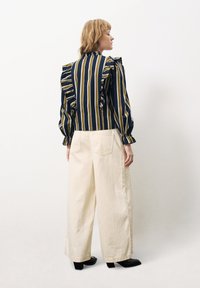 Blouse rayée en bleu marine et jaune avec des épaules volantées, associée à un pantalon large crème et des bottes à talons noires.