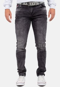 Jeans in denim grigio con vestibilità slim e leggera scoloritura. Presentano cinque tasche, passanti per cintura e sono abbinati a scarpe bianche.