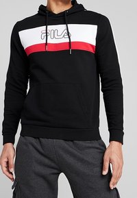 Sudadera negra con franjas horizontales blancas y rojas, con el logo de 'FILA' en el centro. Incluye bolsillo canguro y capucha con cordón ajustable.
