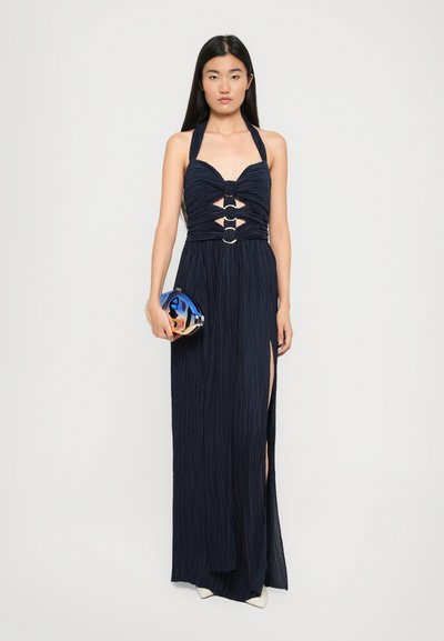 Navy halter maxi dress with pleated fabric, cutouts at the bust, and two front slits. Paired with a shiny blue metallic clutch.