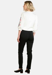 Felpa bianca con ricami floreali sulle maniche, abbinata a pantaloni neri aderenti e scarpe nere, vista da dietro.