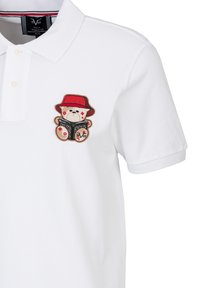 Witte poloshirt met een geborduurde beer die een rode hoed draagt en een boek vasthoudt met zwarte en rode accenten. Zachte stof en klassiek ontwerp.