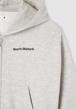 Felpa grigia con zip e scritta "Non Disturbare" in font nero. Presenta una tasca, una texture morbida e un design della cappuccio rilassato.