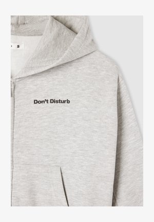 Felpa grigia con zip e scritta "Non Disturbare" in font nero. Presenta una tasca, una texture morbida e un design della cappuccio rilassato.