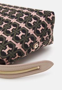 Gros plan d’un sac en tissu à motifs avec des formes géométriques roses et vert foncé, doté d’une sangle en cuir beige et d’une fermeture éclair dorée.