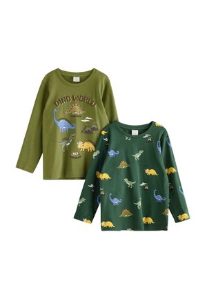 Ung dreng står iført grøn langærmet trøje med dinosaurmønster og matchende bukser med hvide sneakers mod en ensfarvet baggrund.